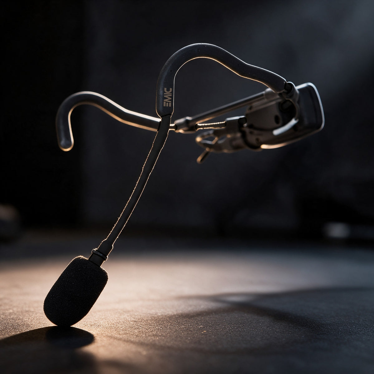Black EMic headset with the MTU8 mini transmitter mounted behind the ear on its bracket, lit from the side in a dim studio
