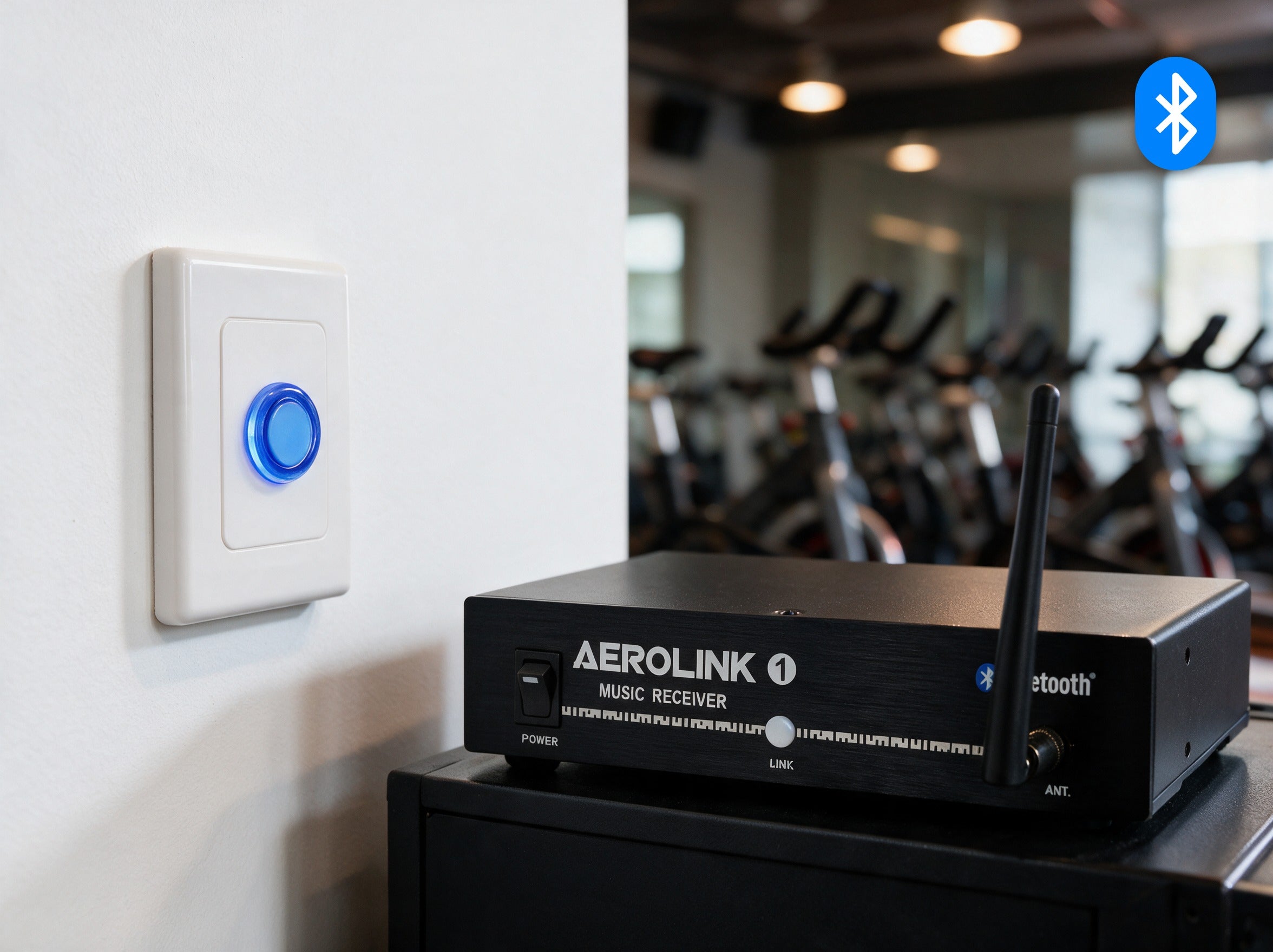 AeroLink 1 Bluetooth music receiver with front antenna on an AV cabinet, below a wall pairing button lit blue in an indoor cycling studio