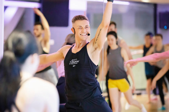Instructor in a black tank top leading a fitness class with a blurred background, wearing the yellow Aeromic headset.