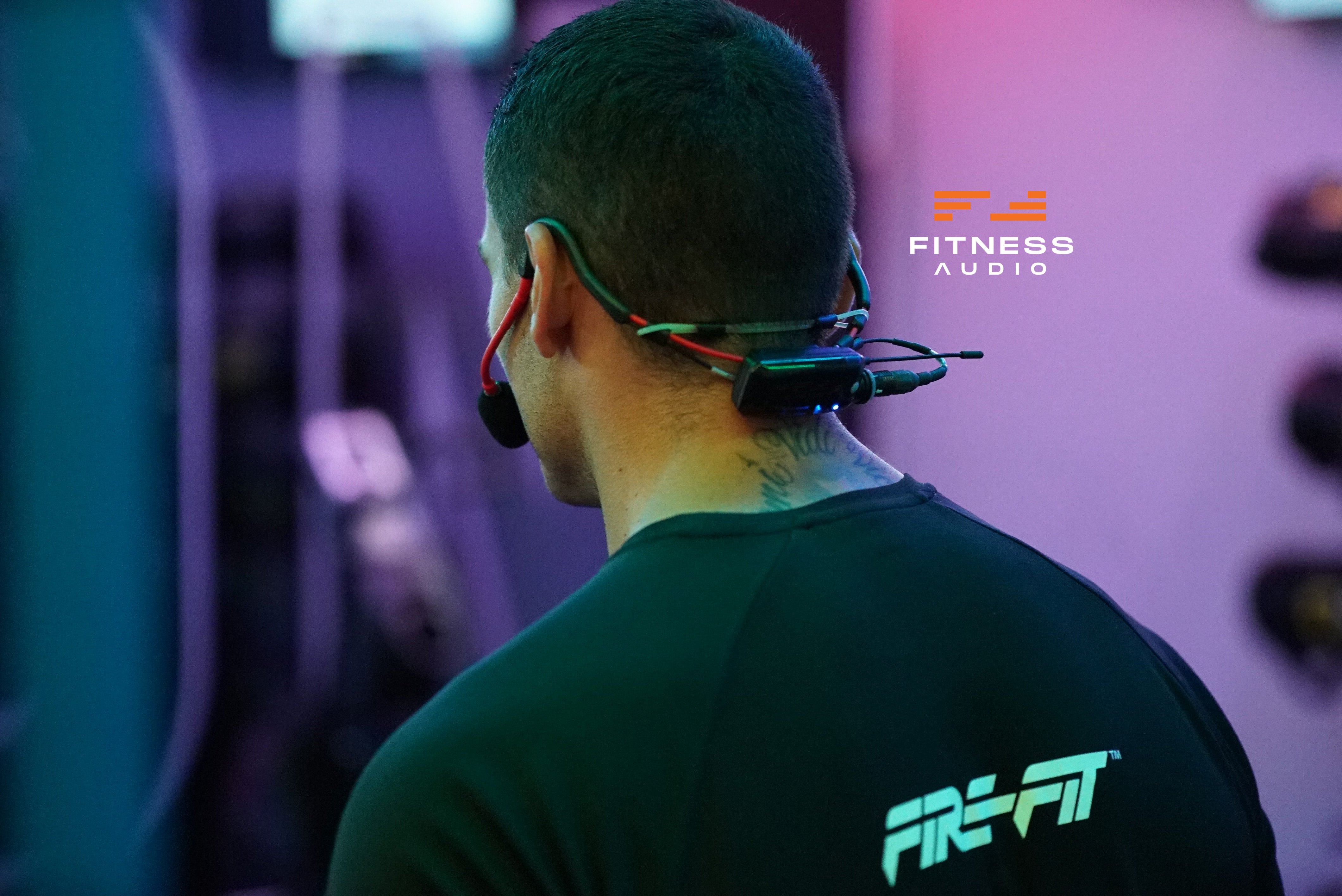 Instructor wearing a wireless MTU8 system with 'Fitness Audio' branding in a blurred indoor setting.