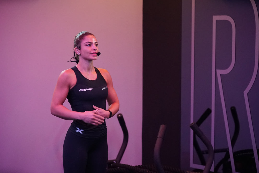 Instructor in athletic wear standing on a stage with exercise equipment in the background, and the MTU8 and Emic headset on her head.