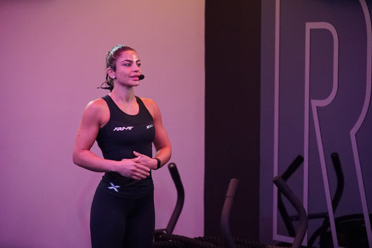 Instructor in athletic wear standing on a stage with exercise equipment in the background, and the MTU8 and Emic headset on her head.